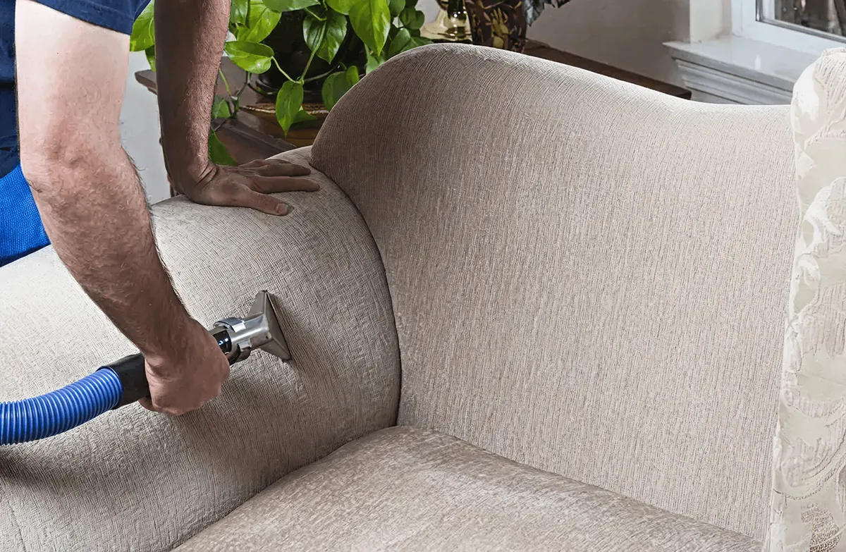 Professional upholstery cleaner deep-cleaning a fabric sofa with a handheld extraction tool and hose, Cincinnati, OH.